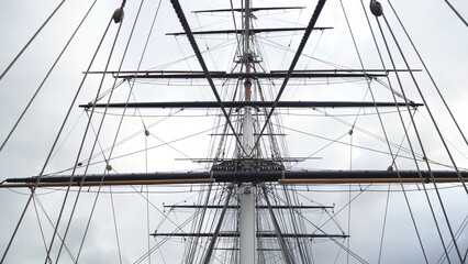 Obraz premium Masts and cables of ship on background of cloudy sky. Action. Towering masts with many intertwined cables and ropes of sailing ship on background of cloudy sky