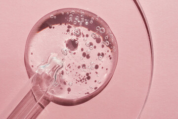 Pipette with sample of gels cosmetic product in petri dish on pink background, hard shadows