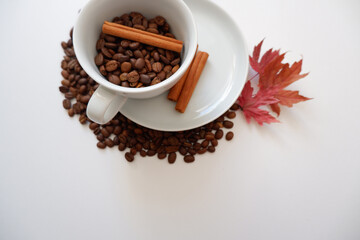 Roasted coffee beans composition with cinnamon sticks and maple leaves on white background. Seasonal drink image concept background. 