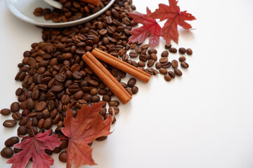 Roasted coffee beans composition with cinnamon sticks and maple leaves on white background. Seasonal drink image concept background. 