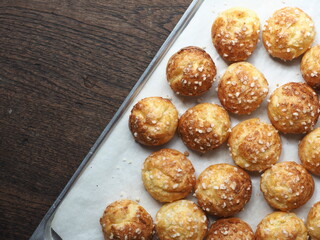 top view chouquettes coated with pearl sugar on baking tray on wooden background