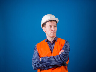Road worker. A guy in a construction helmet and an orange vest. Studio shooting on a blue background