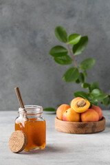  A jar with apricot jam and a spoon close-up on a gray. Fruit preservation.