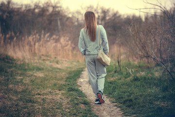 a slender girl in a tracksuit walks along the path of the park in early spring