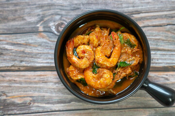 Close up of Stir fried shrimp and red curry paste in a black bowl on wood table. Thai food made