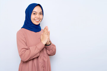 Smiling beautiful Asian muslim woman in casual shirt gesturing eid mubarak greeting isolated over white background. People religious lifestyle concept