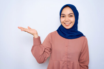 Smiling young Asian muslim woman in pink shirt showing copy space on palm isolated over white background. People religious lifestyle concept