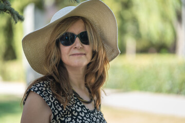 Woman in straw hat and sunglasses outside a public park on a sunny day.
