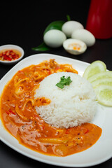 Rice topped with salted egg fried squid in a white plate on a black table.