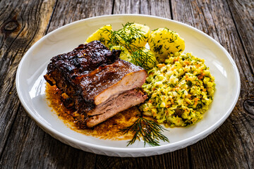 Tasty roast ribs with boiled potatoes and coleslaw on wooden table
