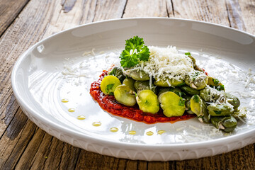 Broad beans salad in tomato sauce with parmesan on wooden table
