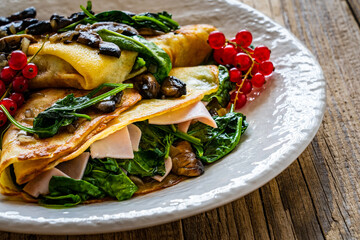 Crepes with spinach, fried mushrooms and pork ham on wooden table