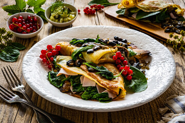 Crepes with spinach, fried mushrooms and pork ham on wooden table