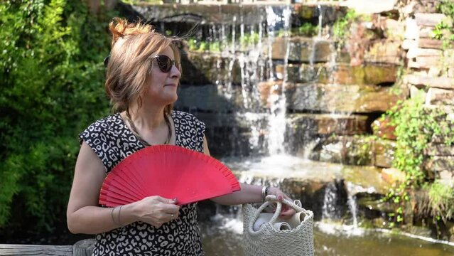 Woman fanning slowly with a small waterfall of fresh water in the background, slowmotion.
