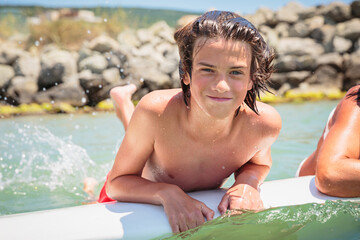 Handsome teenage boy lying on a swimming board and having fun floating on a swim board in the sea on a hot summer day