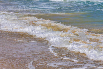 Foam and splashes on coastal waves. Sandy beach of the Mediterranean Sea.