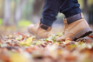Autumn concept. Pedestrian feet on the road. Autumn leaves on the footpath.