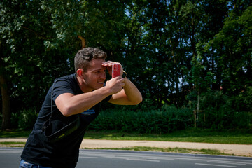 A male trying to take a photo with a phone outdoors in the park under the sunlight