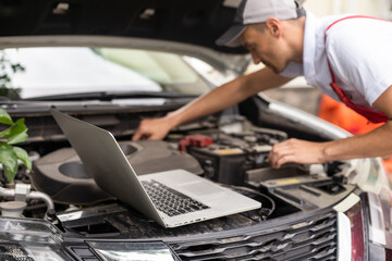 Naklejka premium Mechanic with laptop near car engine. Modern car diagnostic program on screen. Car service concept