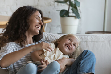 Excited happy mom tickling joyful little daughter, tickling kid, holding child in arms, playing...