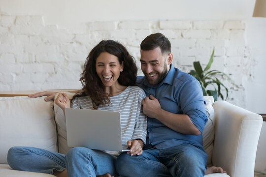 Excited millennial married couple looking at laptop computer screen with winner yes hands, laughing, shouting for joy, celebrating success, achieve, winning prize, money, learning good happy news