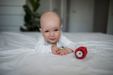 newborn baby holding red wooden toy in mouth while lying on bed in bedroom, baby 6 months old playing with wooden rattle, childhood concept