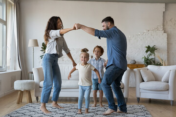 Happy active young parents and little kids playing active games at home together, learning dance to music in living room, holding hands, having fun, celebrating moving, house buying, enjoying party