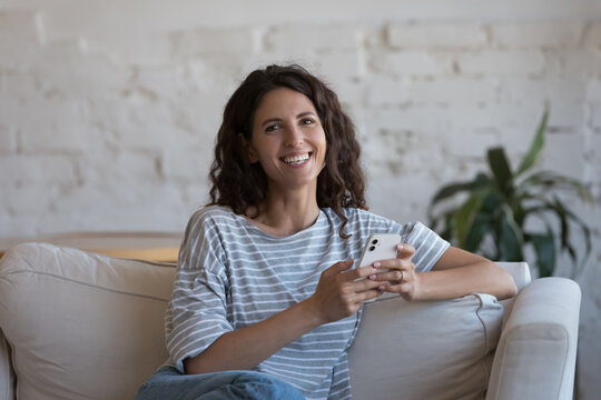 Cheerful beautiful mobile phone user woman head shot indoor portrait. Happy millennial pretty girl holding cellphone, using internet app, online media service, looking at camera with toothy smile