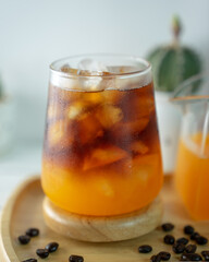 Close up of iced coffee with orange juice, placed on a wooden tray decorated with coffee beans, and...