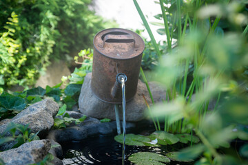 An old, rusty watering can in the form of a fountain on an artificial pond.