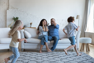 Two active sibling kids running around tired parents, playing active games. Mom and dad exhausted...