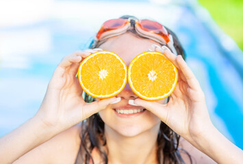Lovely Teen girl standing in swimming outdoor pool showing slices of oranges like glasses