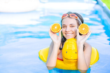 Happy teen girl in swimming pool with inflatable toy duck holds orange. Empty space for text