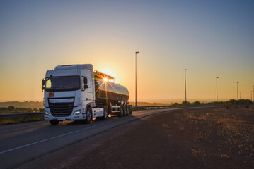 Tanker truck with dangerous goods driving along a lonely road with the sun in backlight
