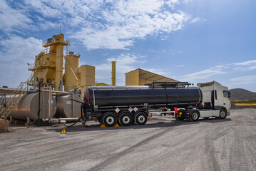 Tanker truck with dangerous goods unloading bitumen in an asphalt plant.