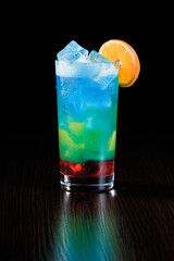 Multicolored blue-green carbonated drink with red jam and ice. Side view, selective focus.