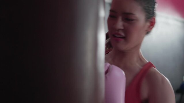 Attractive, young asian athlete woman exercise in sport club. Beautiful sport girl boxer wearing pink gloves training workout punch the sandbag in gym fitness class. Healthy lifestyle concept.