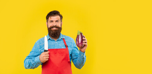 Happy man in apron holding cooks knife and eggplant yellow background copy space, cook