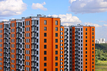 New residential buildings with orange lining on background of green park and blue sky with white clouds. House development, high-rise construction in ecologically clean area