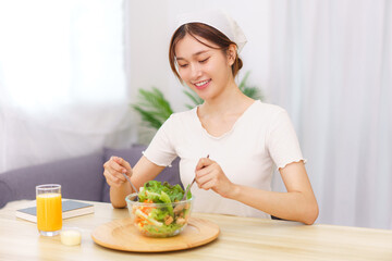 Obraz na płótnie Canvas Lifestyle in living room concept, Young Asian woman mixing vegetable salad in bowl for breakfast
