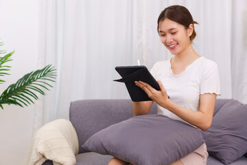 Lifestyle in living room concept, Young Asian woman writing data on tablet while sitting on couch