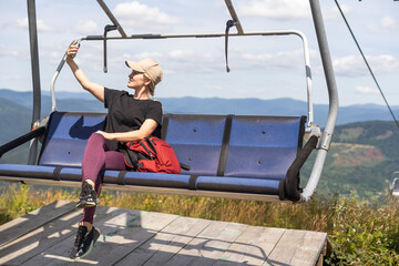 Young women sit on the Chairlift. They take pictures with smartphones. View from the back. Green...