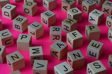 Wooden cubes with letters scattered randomly on a pink background