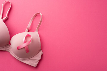 Breast cancer awareness concept. Top view photo of pink ribbon attached to brassiere on isolated pink background with copyspace