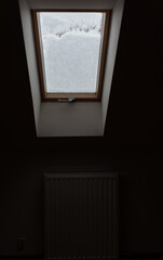 Roof window covered with snow. The snow on the glass blocks the light in a dark room.