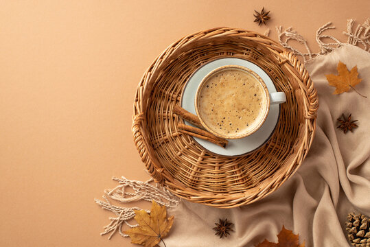 Autumn concept. Top view photo of wicker basket with cup of frothy coffee on saucer cinnamon sticks anise autumn maple leaves pine cone and plaid on isolated beige background
