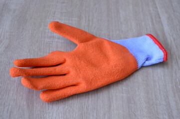 Orange rubber work glove on wooden background, protective equipment