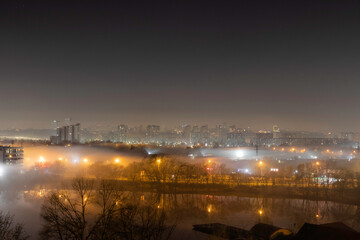 Night cityscape of the big city. Awesome bright, multi colored light in thick fog at empty streets. Apartment buildings in bedroom community, commuter town area. Darnytsia, Kyiv. Ukraine. 2021