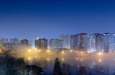 Night cityscape of the big city. Awesome bright, multi colored light in thick fog at empty streets. Apartment buildings in bedroom community, commuter town area. Darnytsia, Kyiv. Ukraine. 2021
