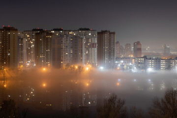 Night cityscape of the big city. Awesome bright, multi colored light in thick fog at empty streets. Apartment buildings in bedroom community, commuter town area. Darnytsia, Kyiv. Ukraine. 2021